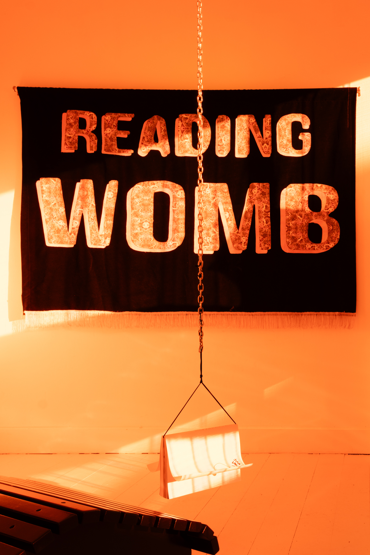 Lyónn Wolf, Big Book of De-production (detail), 2025, artist book, 322 pages, b&w, A4. Lounger, cushions, chain; and Reading Womb, 2025, banner, velvet, custom printed textile, hand dyed textile. Photo: Rita Silva (LYÓNN WOLF  0)