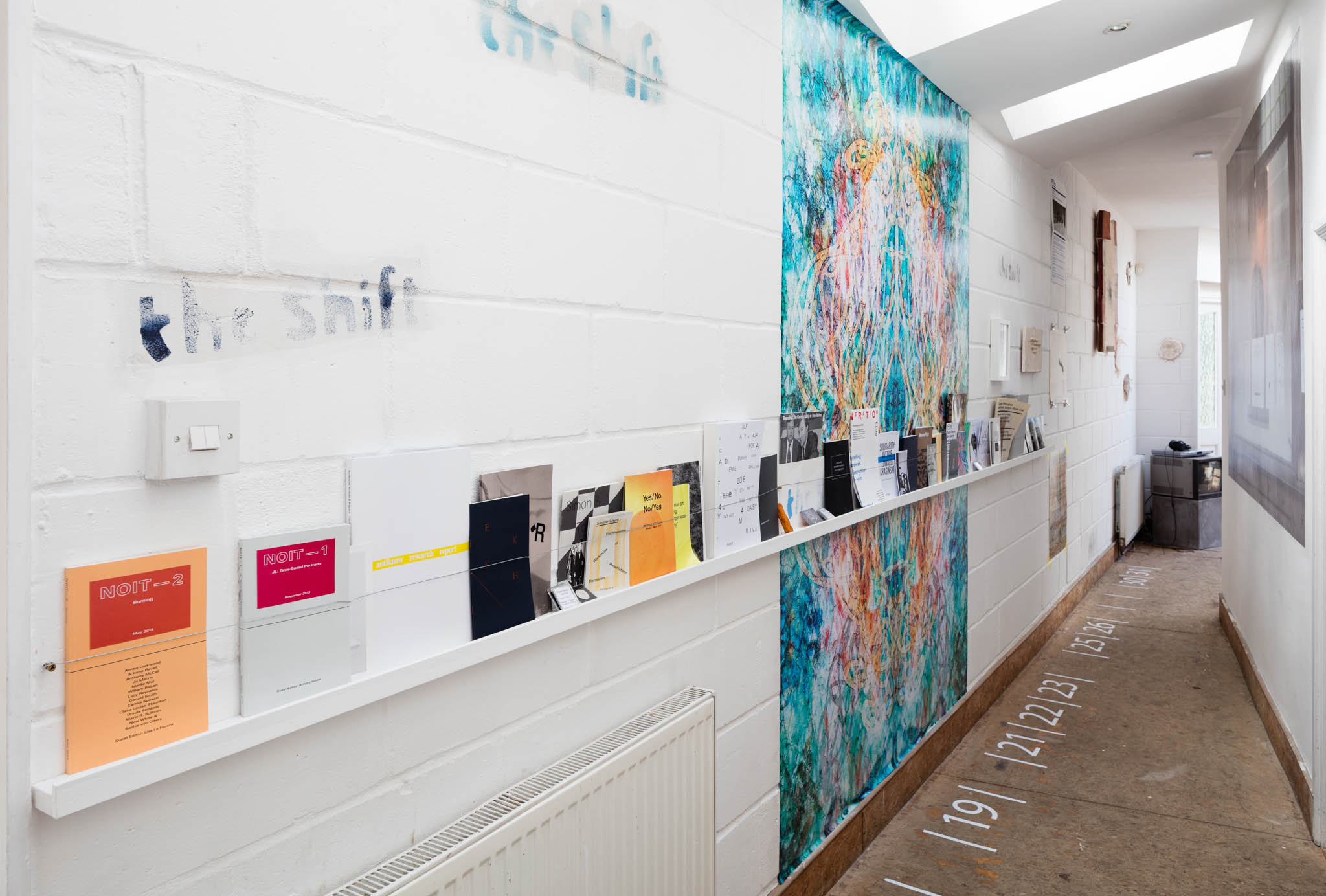 Shelf: Publications produced by FTHo; On wall: Mark Titchner, 'Untitled', 2011; On floor: John Latham, Floor markings from 'The Government of the First and Thirteenth Chair', 1978/1991  (The Shift 8)